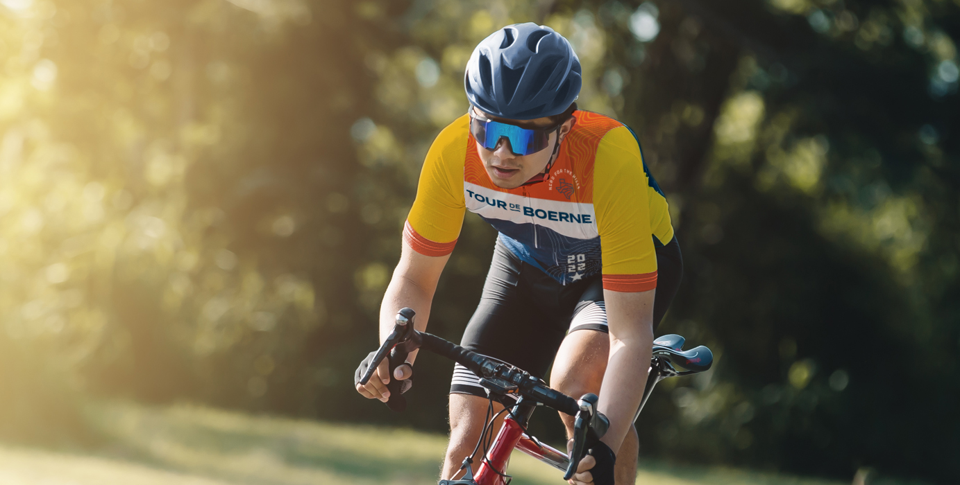 Showing a man riding a bicycle. He is wearing a Tour de Boerne jersey, as he competes in the annual Tour de Boerne bike race in Boerne, TX. Branding designed by MDR for this San Antonio-based organization.