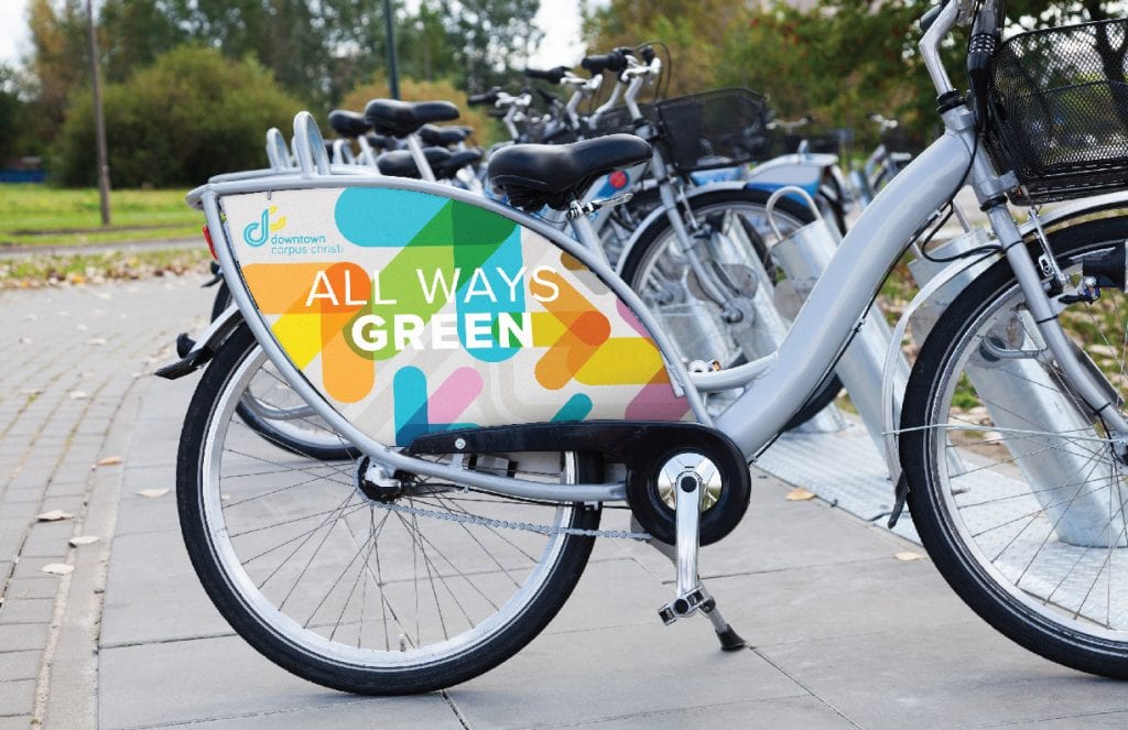 Showing a bicycle with a sign attached to the frame that features an advertisement for Downtown Corpus Christi.